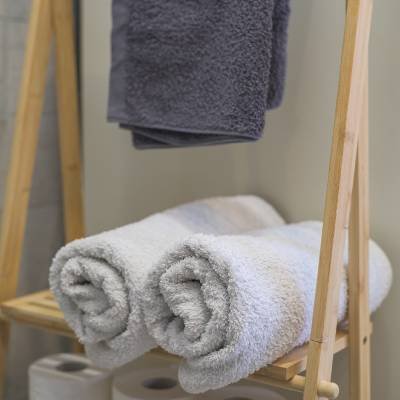 Rolled and folded fresh towels on a wooden ladder shelf next to toilet paper, emphasizing clean bathrooms and essential amenities provided at Panorama Myrtos, Crete.