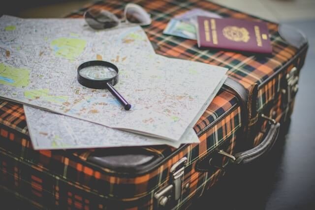 Vintage suitcase with a map, magnifying glass, passport, and sunglasses on top, symbolizing detailed travel planning for a trip to Crete.