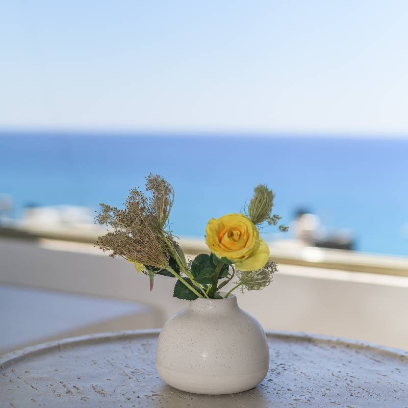 Tranquil Details and Sea Views - Myrtos Apartments Close-up of a decorative flower vase on a balcony table with the deep blue Mediterranean Sea in the background, highlighting the tranquil atmosphere and attention to detail at Panorama Myrtos.